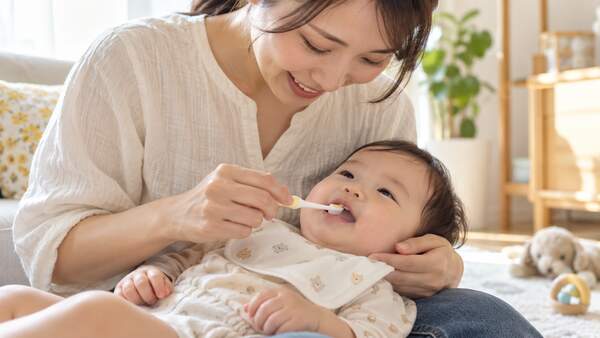 保護者が赤ちゃんの生え始めの乳歯を小さな歯ブラシでみがく様子