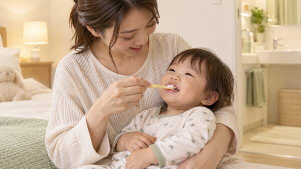 保護者が1歳児を膝に寝かせて仕上げみがきをする様子