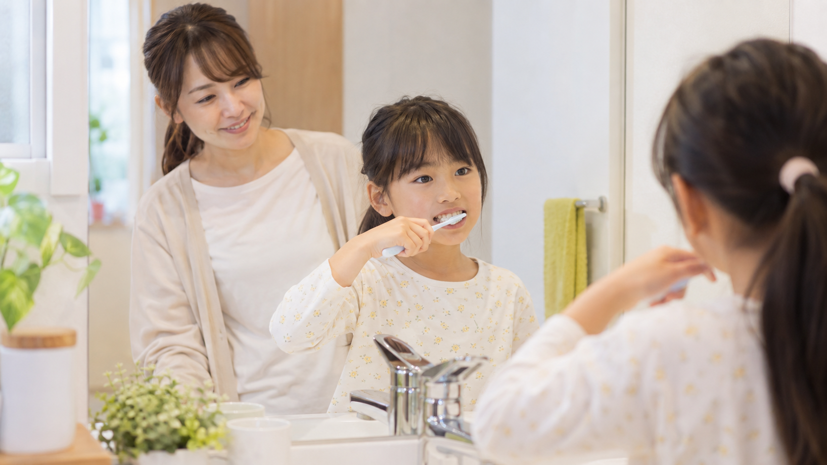 保護者に見守られながら鏡の前で自分の歯をみがく小学生の写真