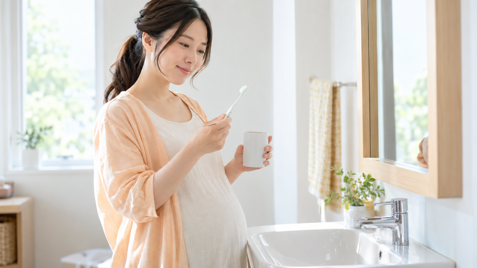小さな歯ブラシとうがい用のコップを持つ妊婦の写真